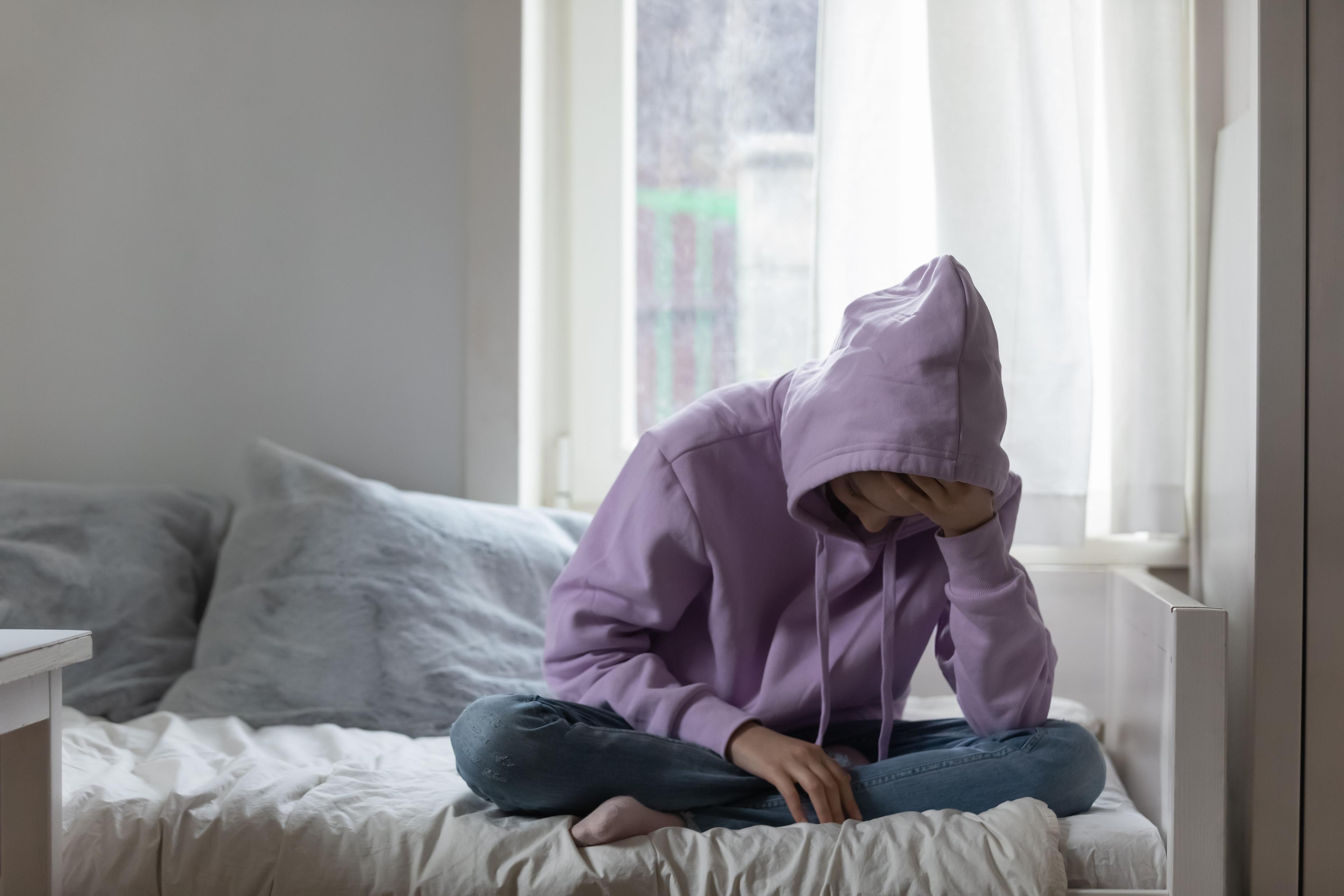 young person in hoodie on bed lookign down |Image credit: @fizkes stock.adobe.com