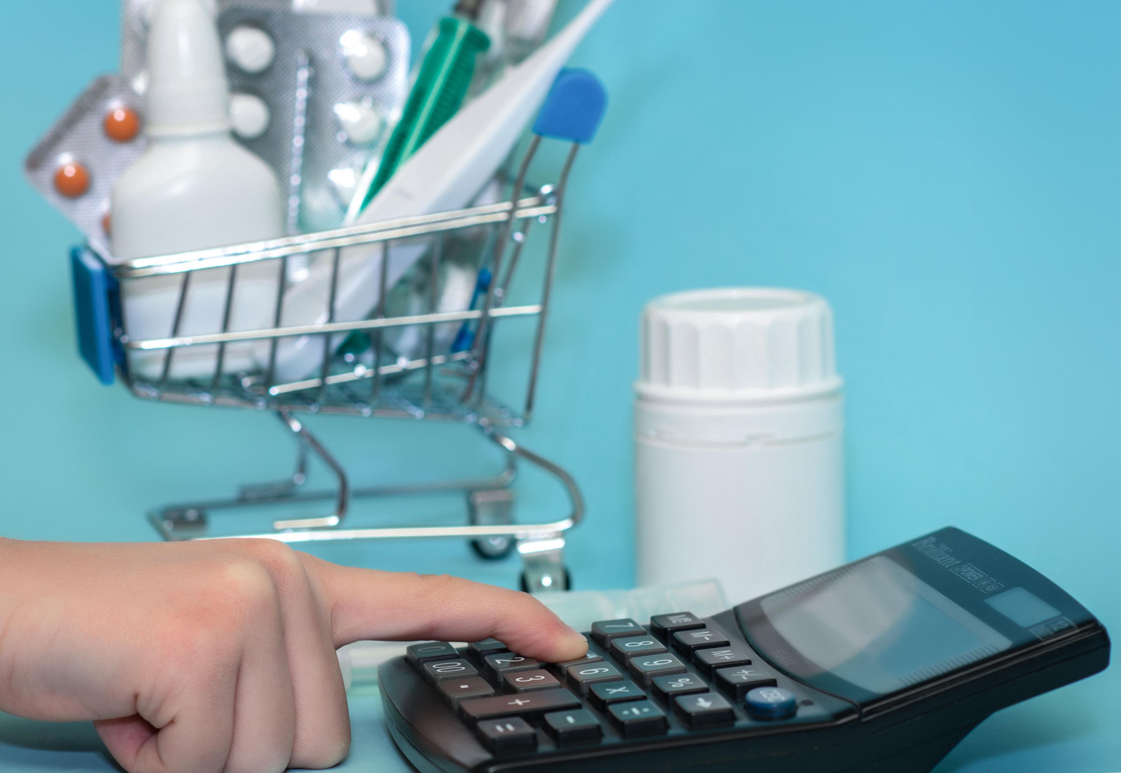 calculator with miniature grocery cart of drugs | Image credit: ©syhin_stats stock.adobe.com