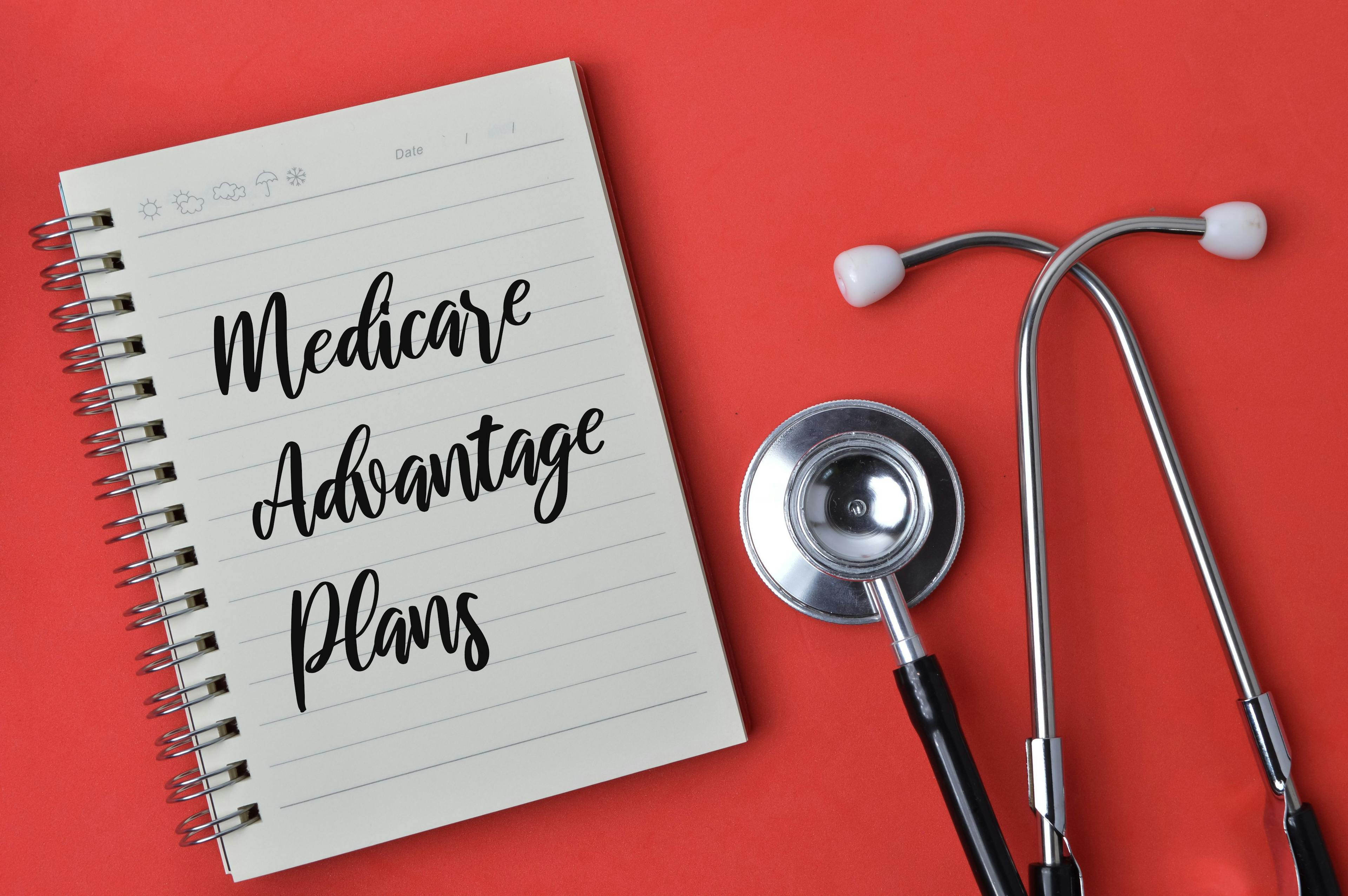 Medicare Advantage written on a pad, pink background, with stethoscope | Image credit: ©TeacherPhoto stock.adobe.com