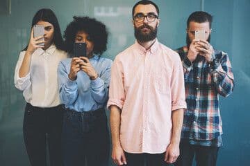 Four people facing ahead, three looking at phones | Image credit: ©Bullrun stock.adobe.com